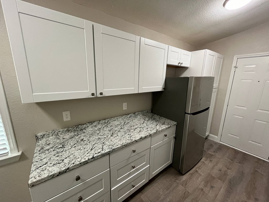 a kitchen with white cabinets and granite counter tops and a stainless steel refrigerator