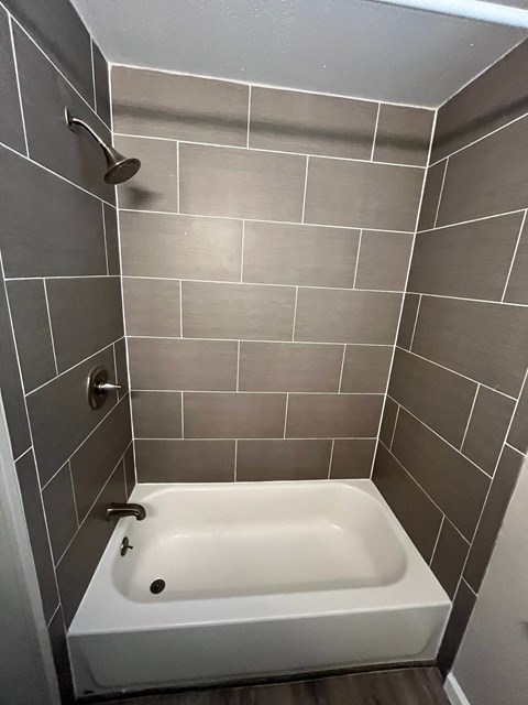 A white bathtub in a bathroom with grey tiled walls.