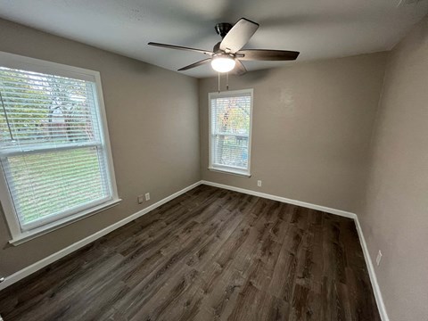 A room with a ceiling fan and two windows.