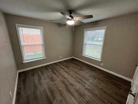 A room with a ceiling fan and two windows.
