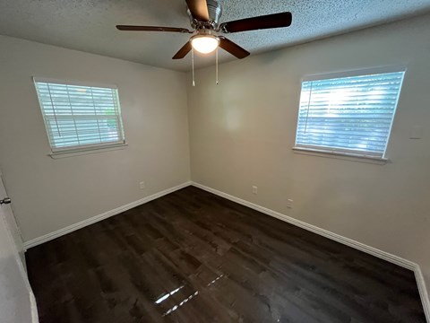 A room with a ceiling fan and two windows.