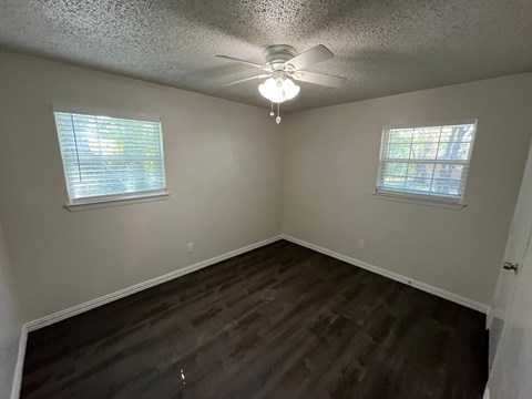 A room with a ceiling fan and two windows.