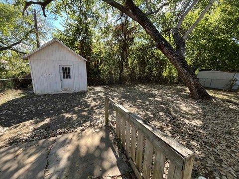A small white shed sits in a yard with a wooden fence.
