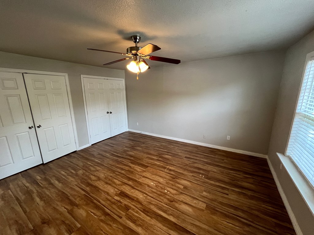 an empty living room with wood floors and a ceiling fan