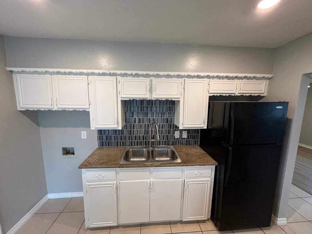 A kitchen with white cabinets and a black refrigerator.