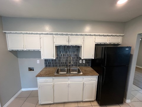 A kitchen with white cabinets and a black refrigerator.
