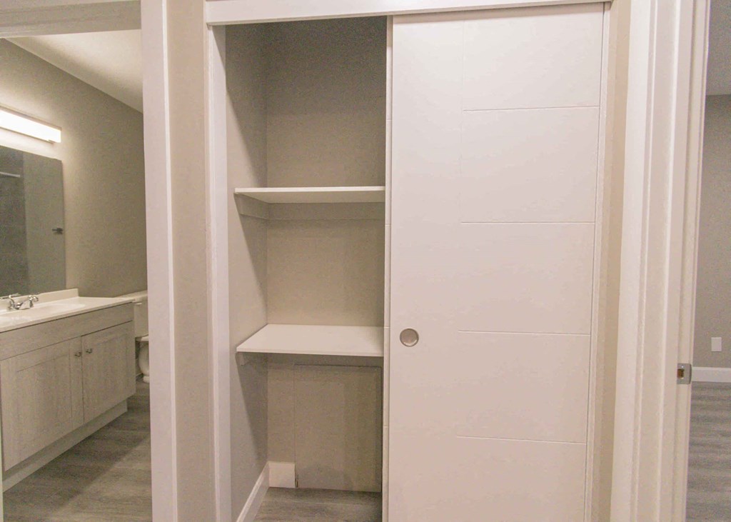a white closet with shelves and a mirror in a bathroom