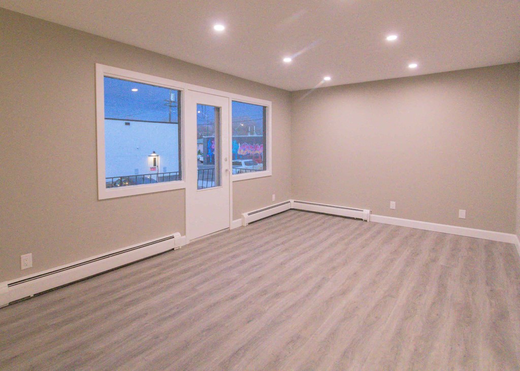 an empty living room with wood flooring and large windows