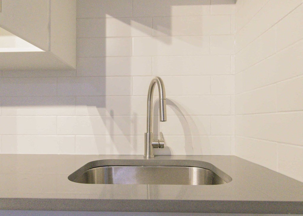 a stainless steel sink in a white tiled kitchen