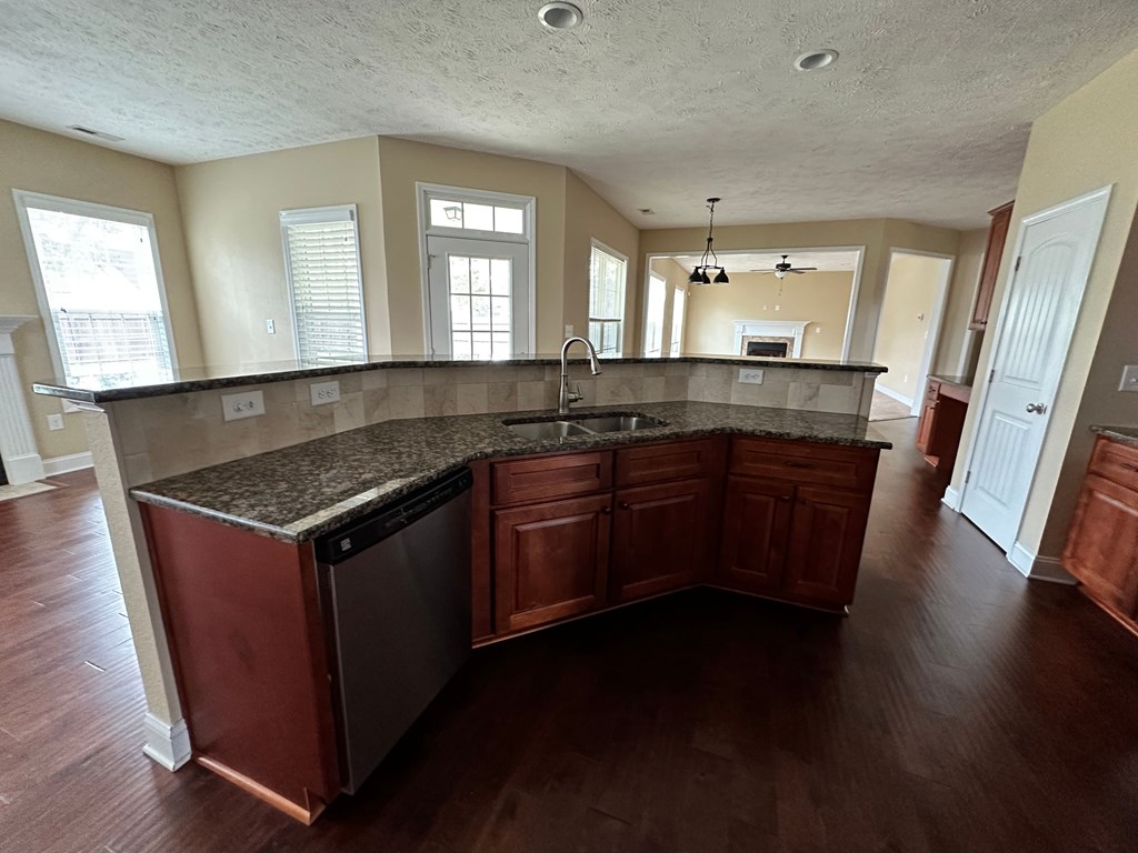 an empty kitchen with granite counter tops and wooden floors