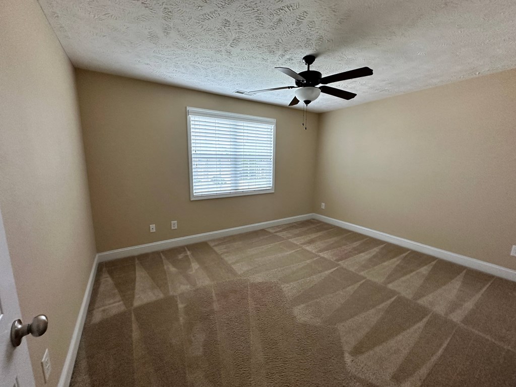 the spacious living room has a ceiling fan and a carpeted floor