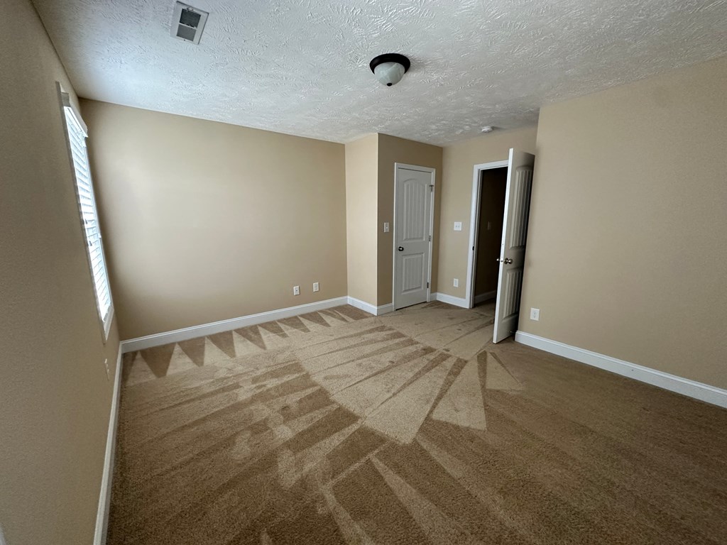an empty living room with carpet and a door to a hallway