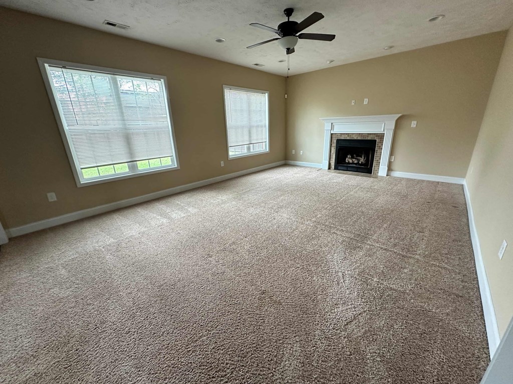 an empty living room with a ceiling fan and a fireplace
