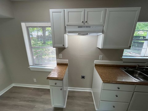 A kitchen with white cabinets and a window with blinds.