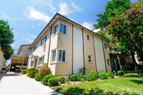 A beige two-story house with a well-maintained lawn and trees in the background.