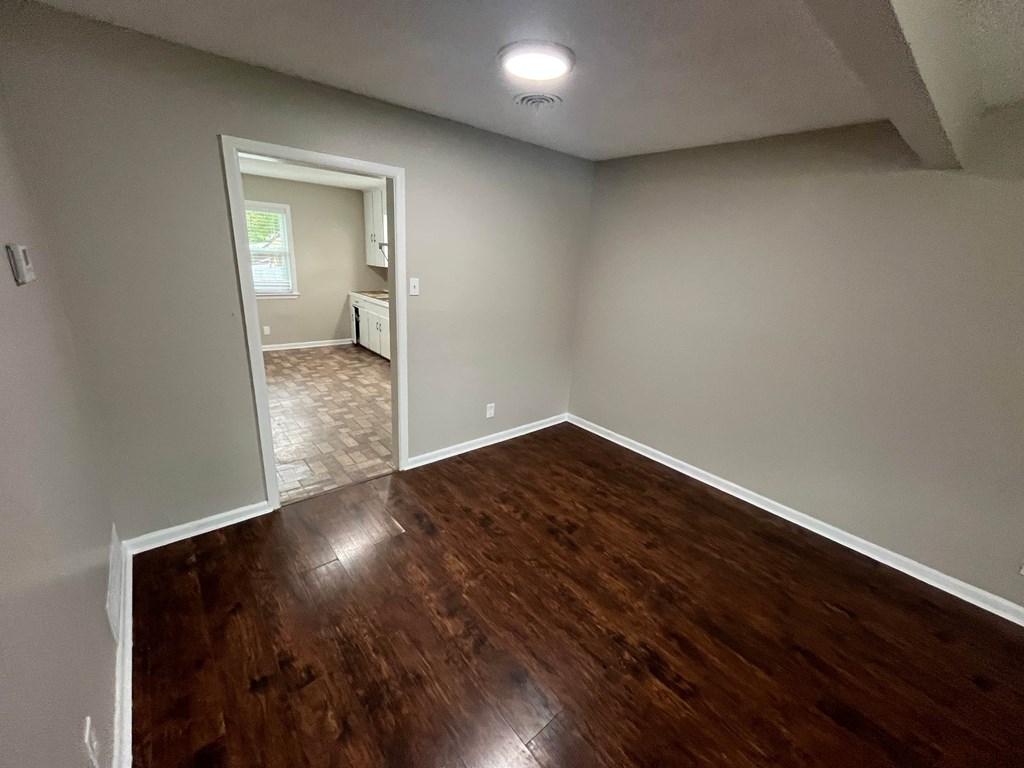 A room with wooden flooring and a doorway leading to another room.