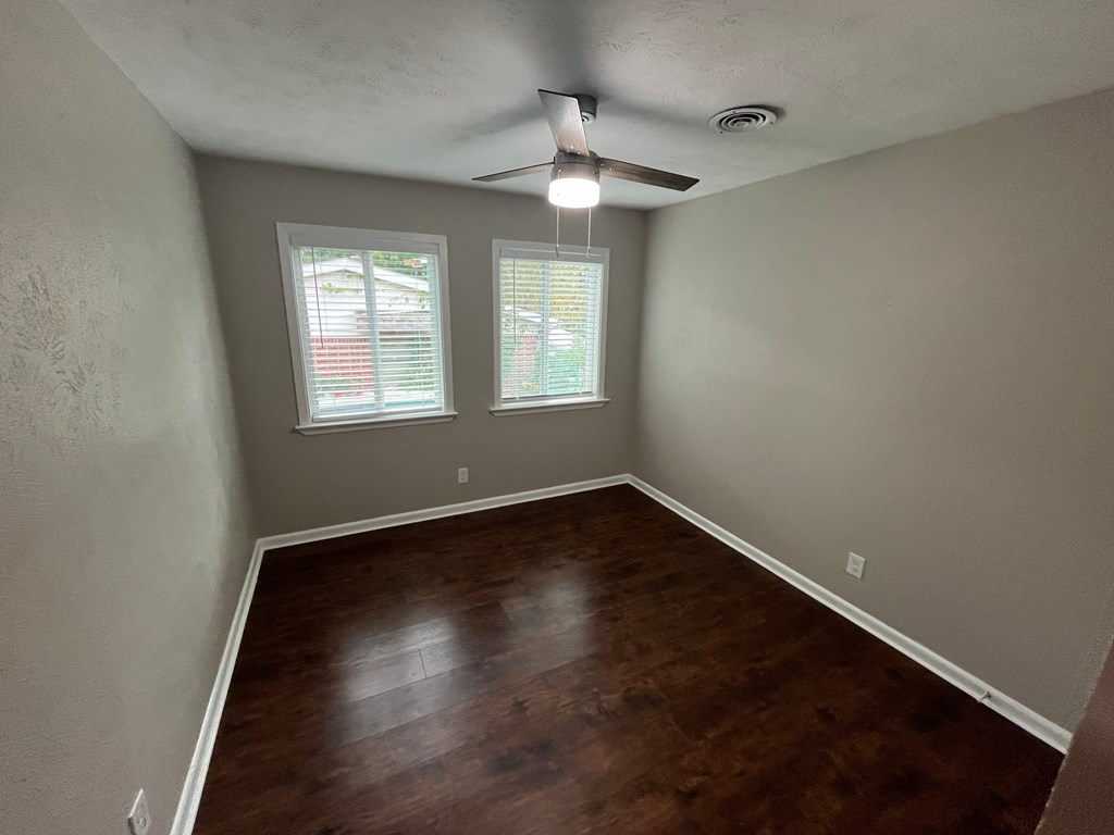 A room with a ceiling fan and two windows.