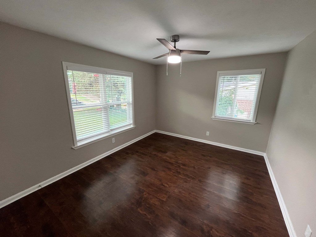 A room with a ceiling fan and two windows.