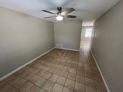 a empty living room with a ceiling fan and tiled floors
