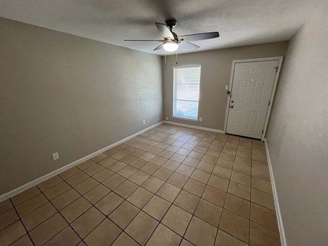 a empty living room with a ceiling fan and tiled floor