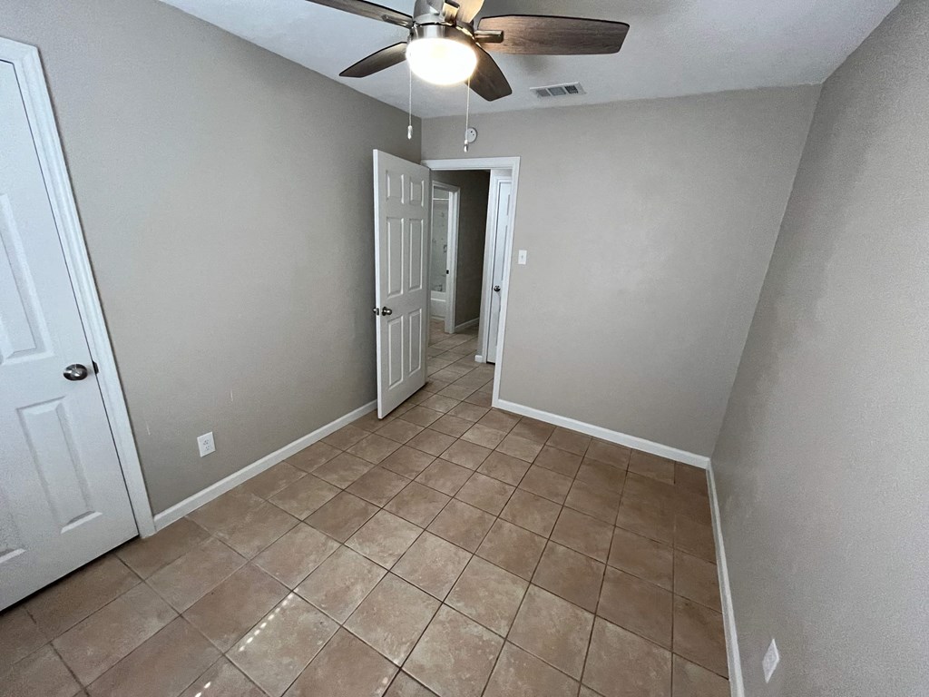 an empty room with a ceiling fan and tiled floors