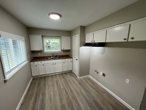 A kitchen with white cabinets and a window with blinds.