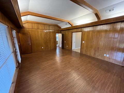 A room with wooden floors and walls, and a window with blinds on the left side.