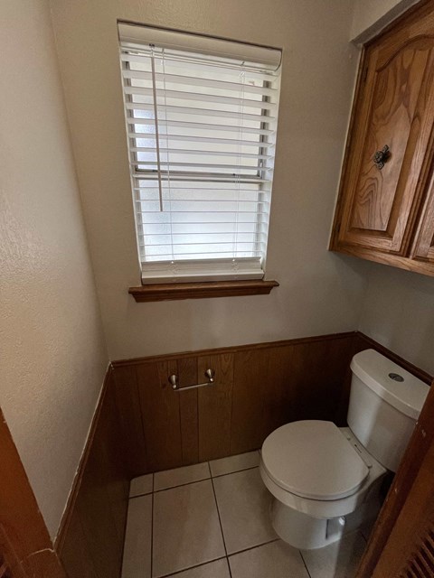 A white toilet sits in a small bathroom with a window above it.