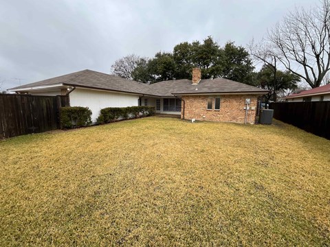 A house with a brown roof and a white wall is surrounded by a grassy yard.