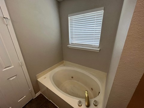 A white bathtub with a window above it in a bathroom.