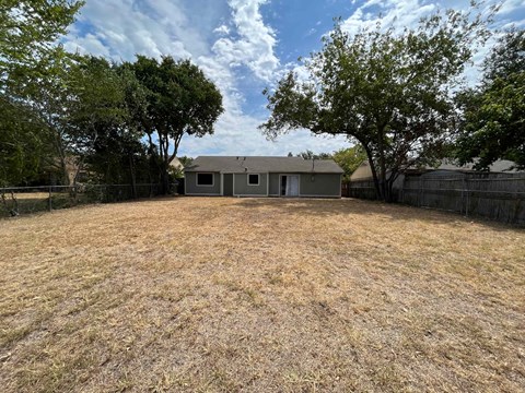 A backyard with a house, trees, and a fence.
