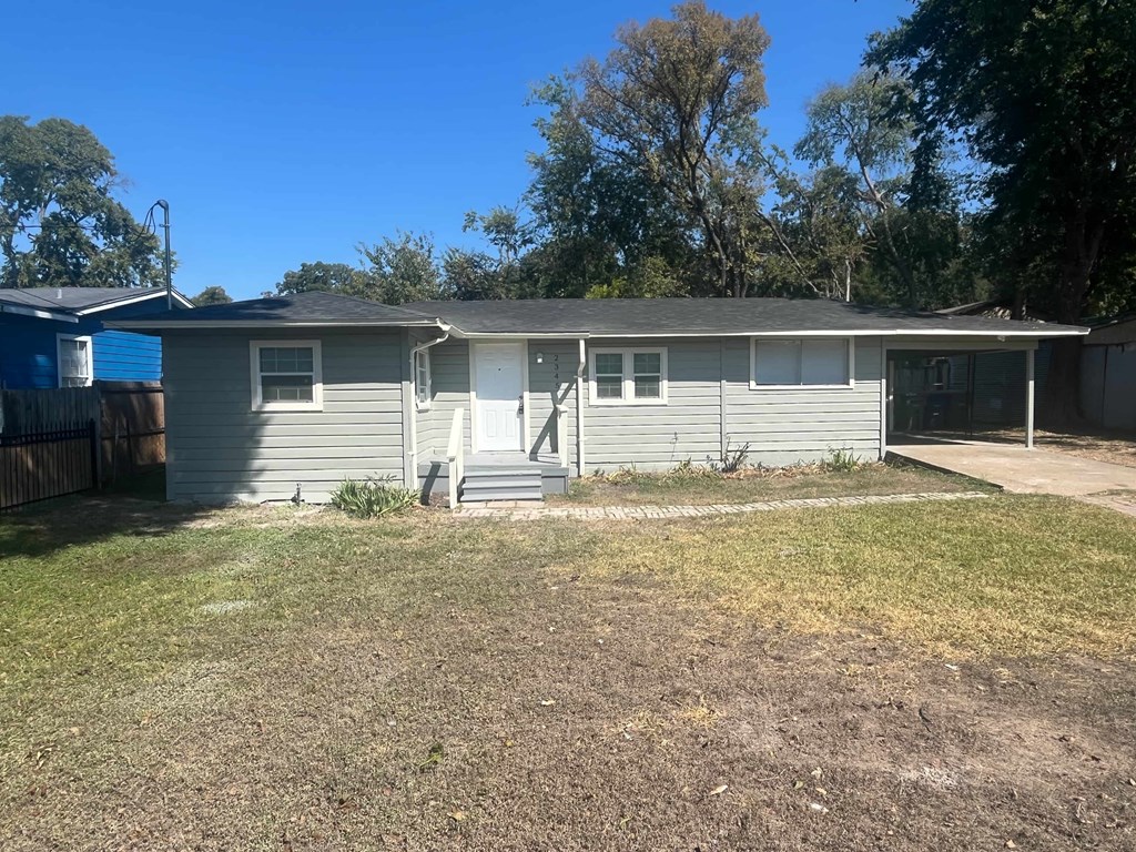 A house with a grey siding and a white door is surrounded by a fence and trees.