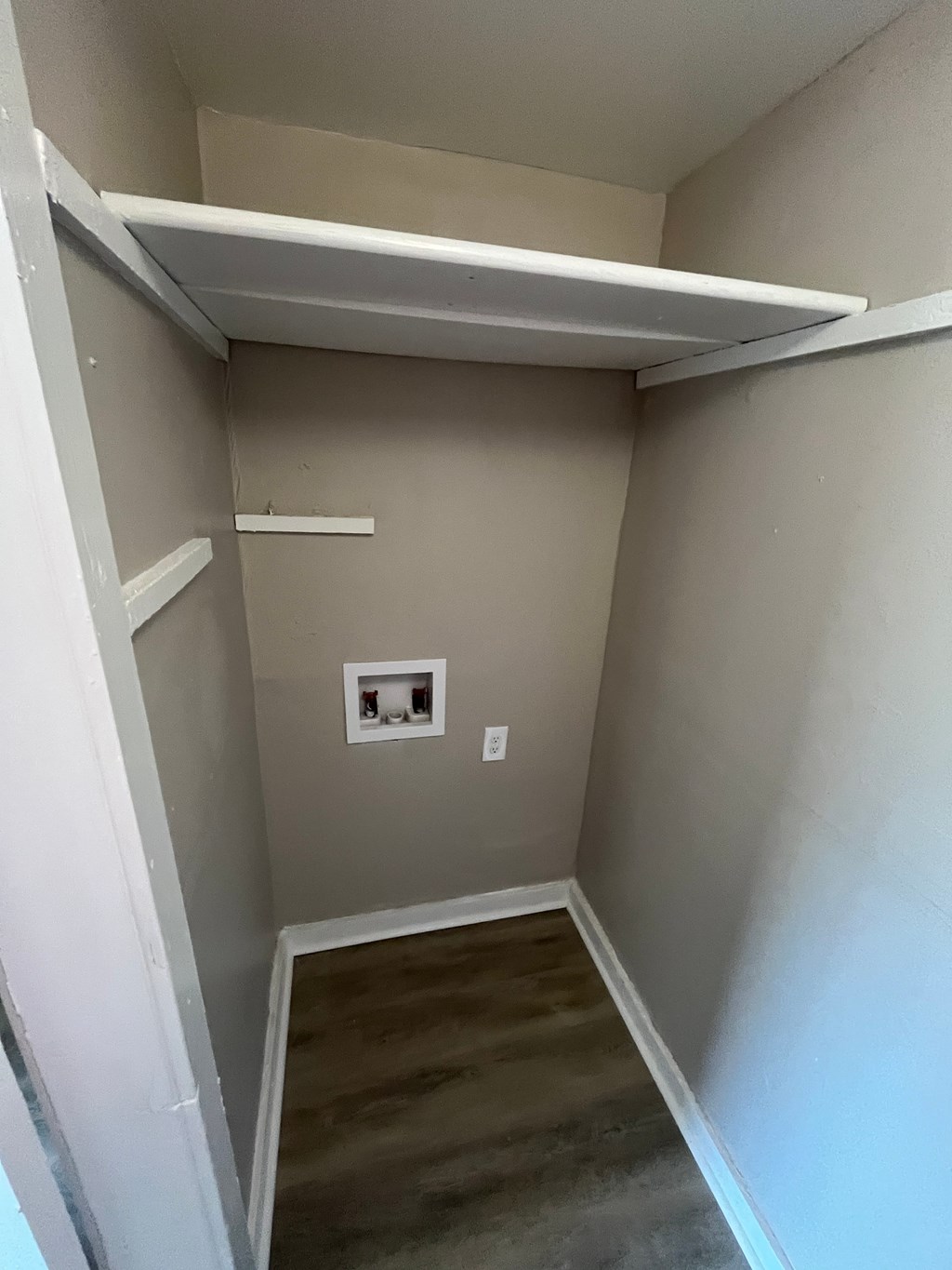 A small, empty room with a single shelf and a light switch on the wall.