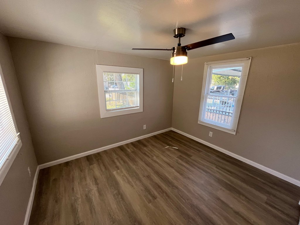 A room with a ceiling fan and two windows.