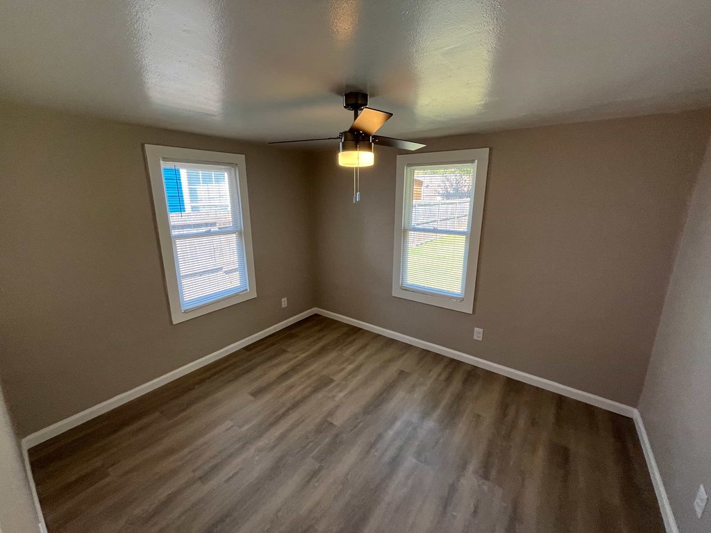 A room with a ceiling fan and two windows.