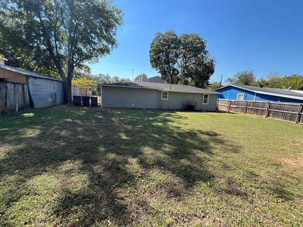 A backyard with a house, a fence, and a tree.