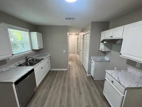 A kitchen with white cabinets and a wooden floor.