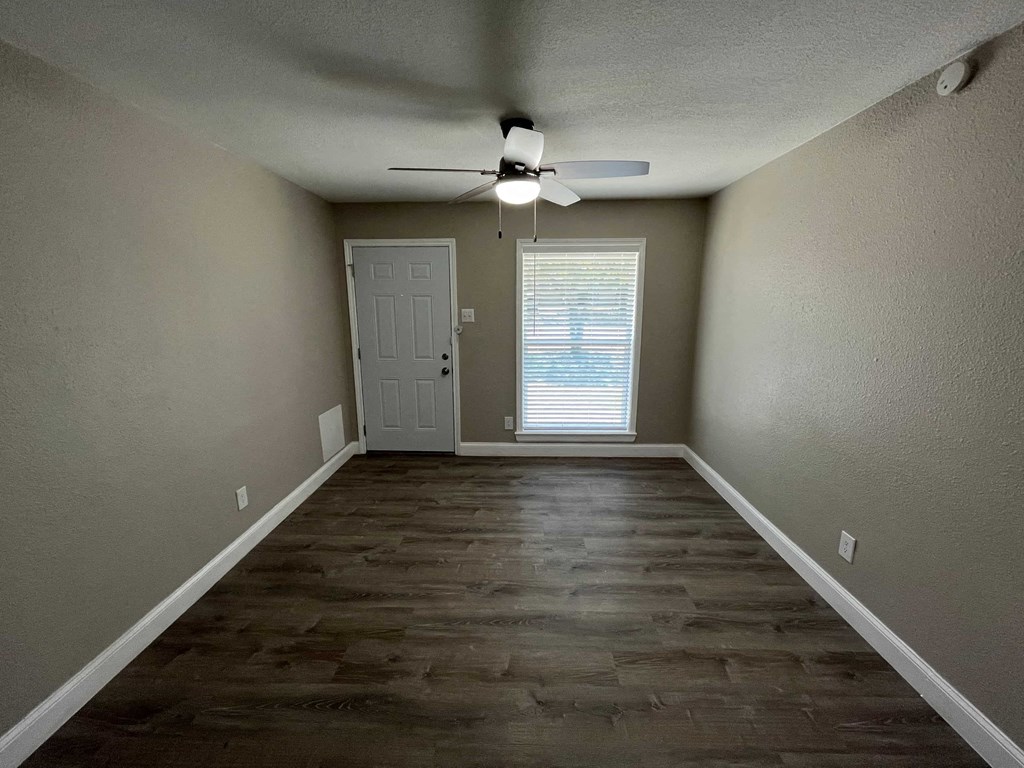 a empty living room with a ceiling fan and a door