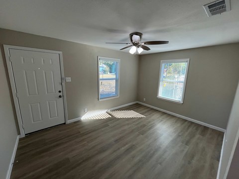 A room with a white door, a ceiling fan, and a window with blinds.