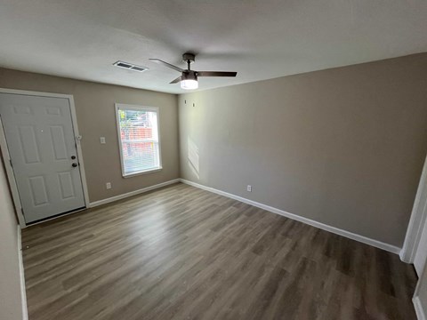 A room with a ceiling fan and light, wooden flooring, and a door.