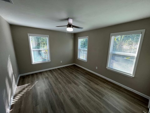 A room with a ceiling fan and two windows.