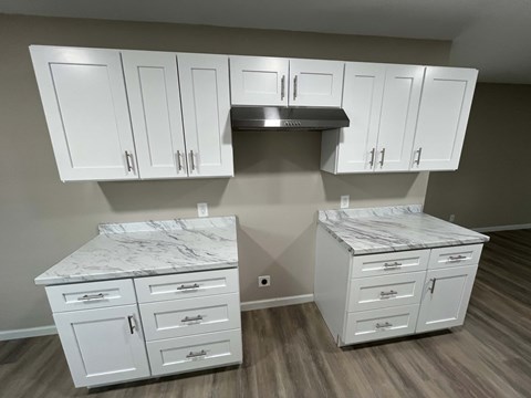 A kitchen with white cabinets and marble countertops.