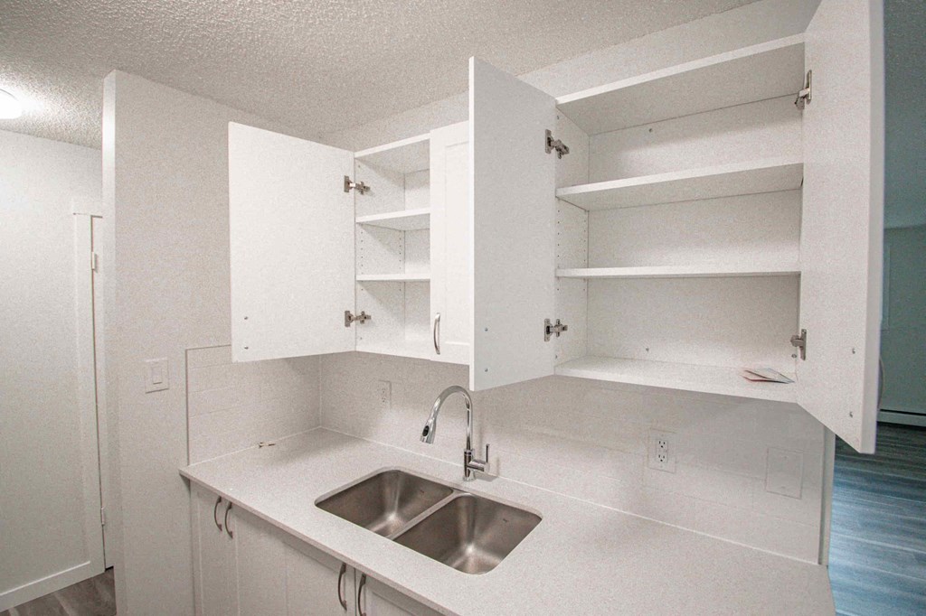 an empty kitchen with a sink and white cabinets
