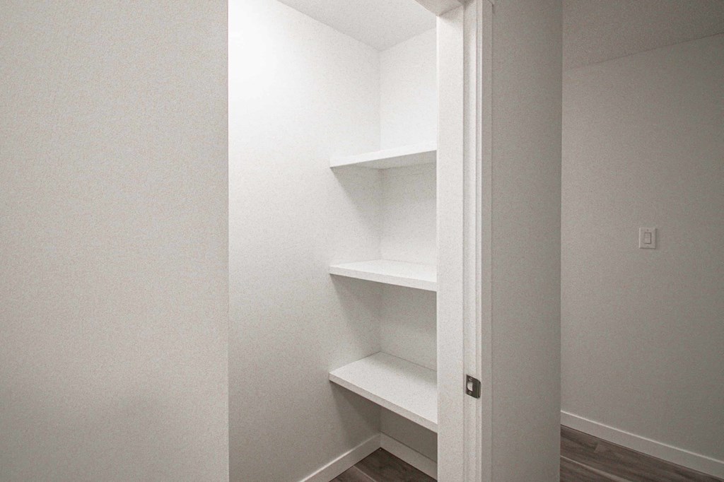 a walk in closet with white shelves and a door
