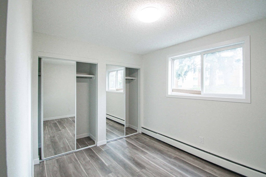 an empty room with white walls and a window and a mirrored closet