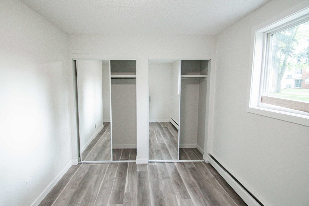 an empty room with white walls and wood flooring and a closet