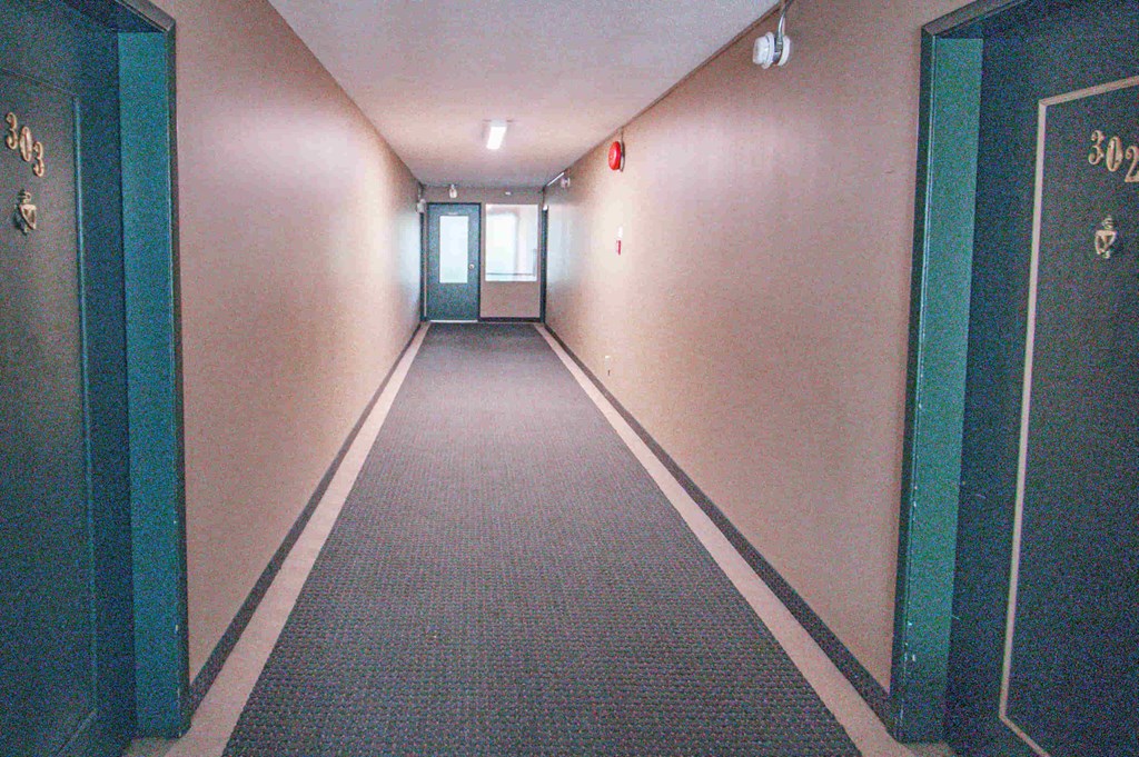 a long hallway with green doors and white walls and a carpet