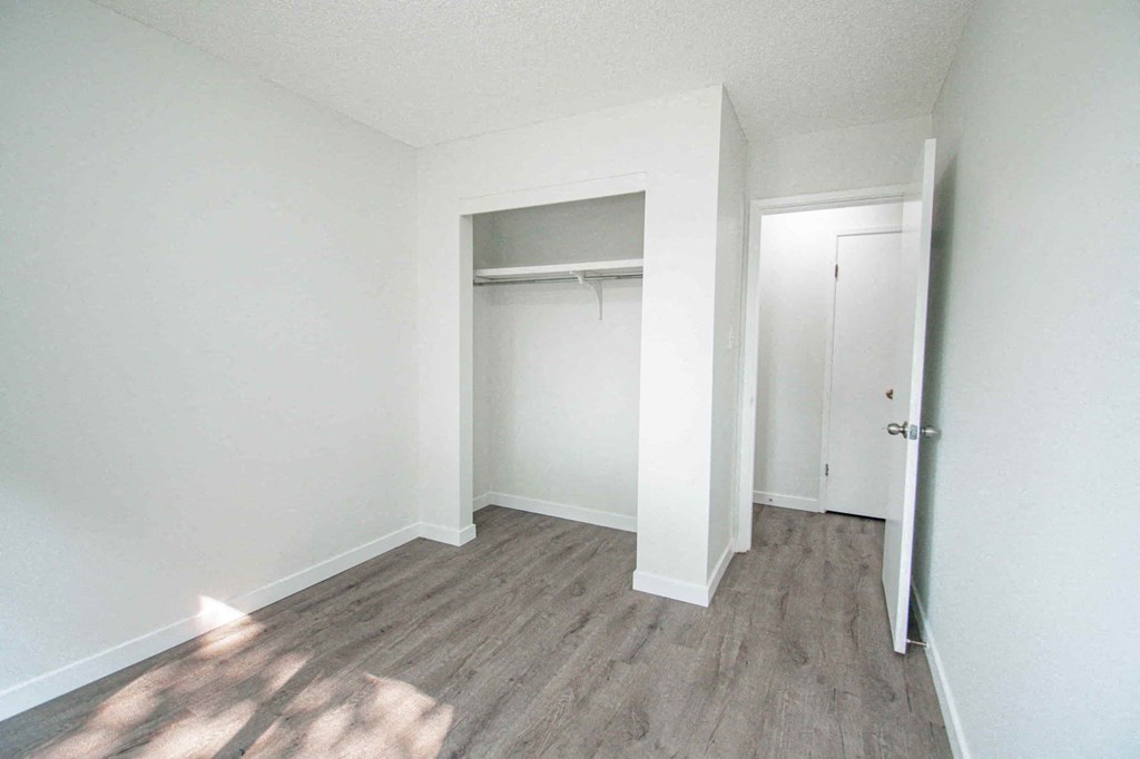 a bedroom with white walls and wood flooring and a closet