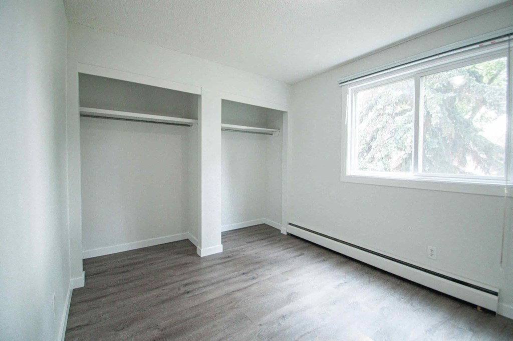 an empty bedroom with white walls and wood floors and a large window