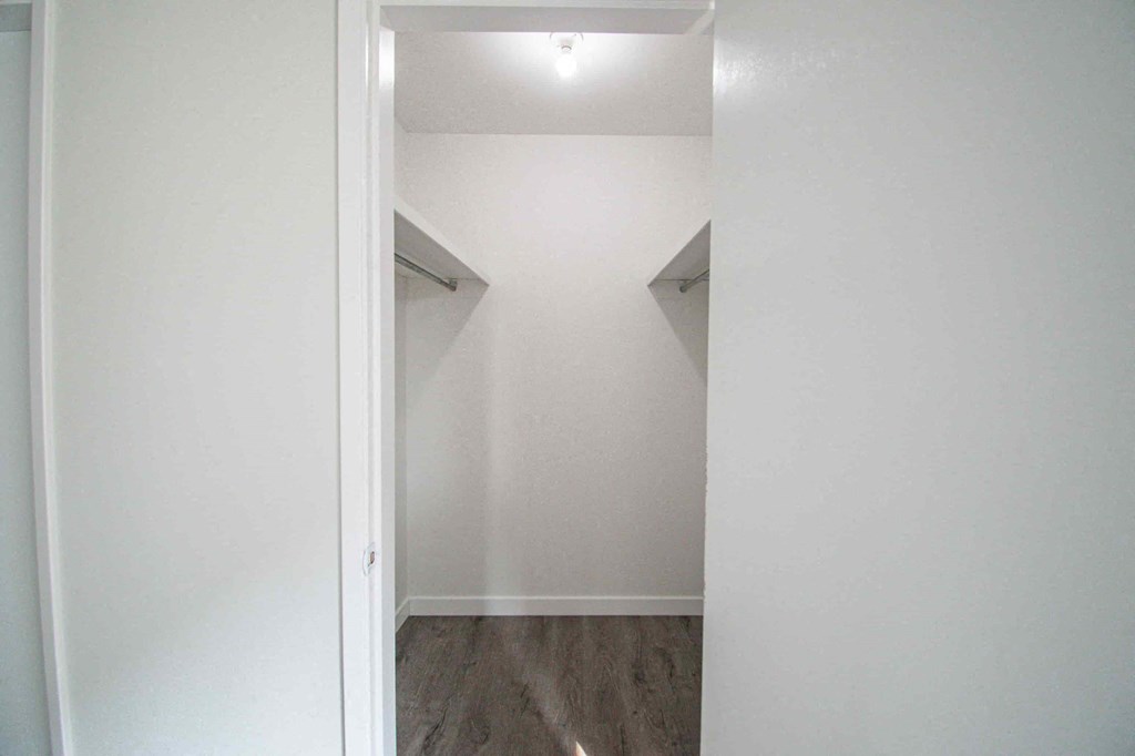 a walk in closet in a room with white walls and a wood floor
